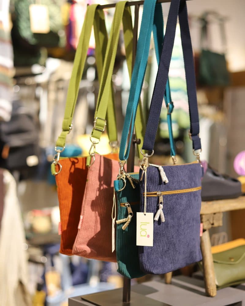 Corduroy and leather crossbody bags hanging on a display stand.